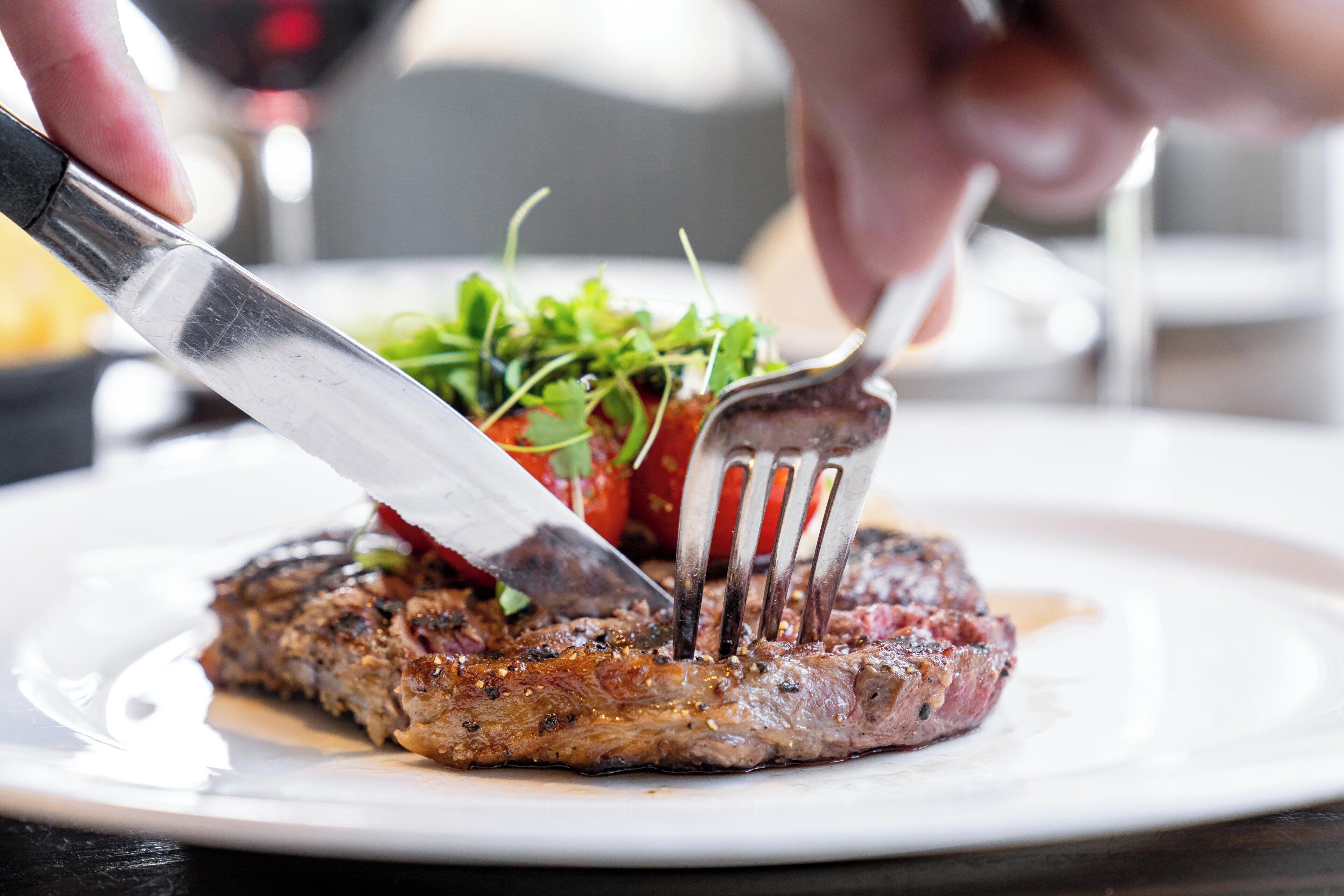 A steak being cut with a knife and fork on a plate.