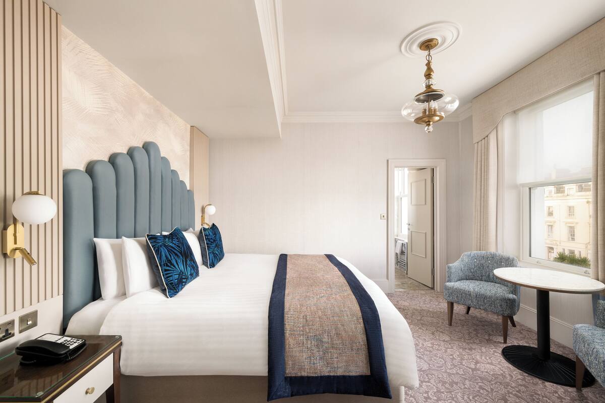 Une chambre d’hôtel avec un grand lit, une table de chevet avec une lampe, une petite table ronde et une chaise.
