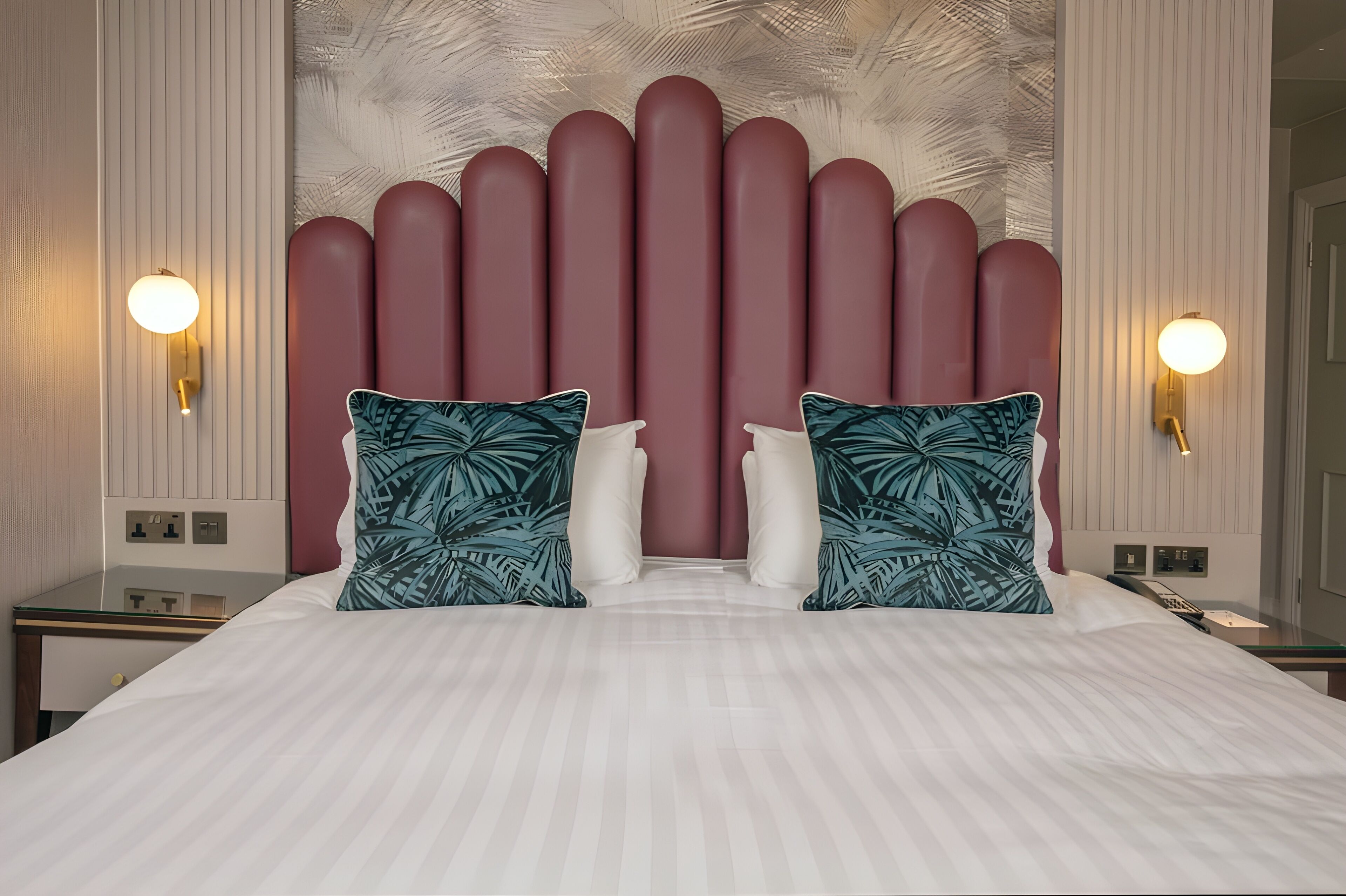 A hotel room with a large bed, two wall-mounted lamps, and a decorative headboard.