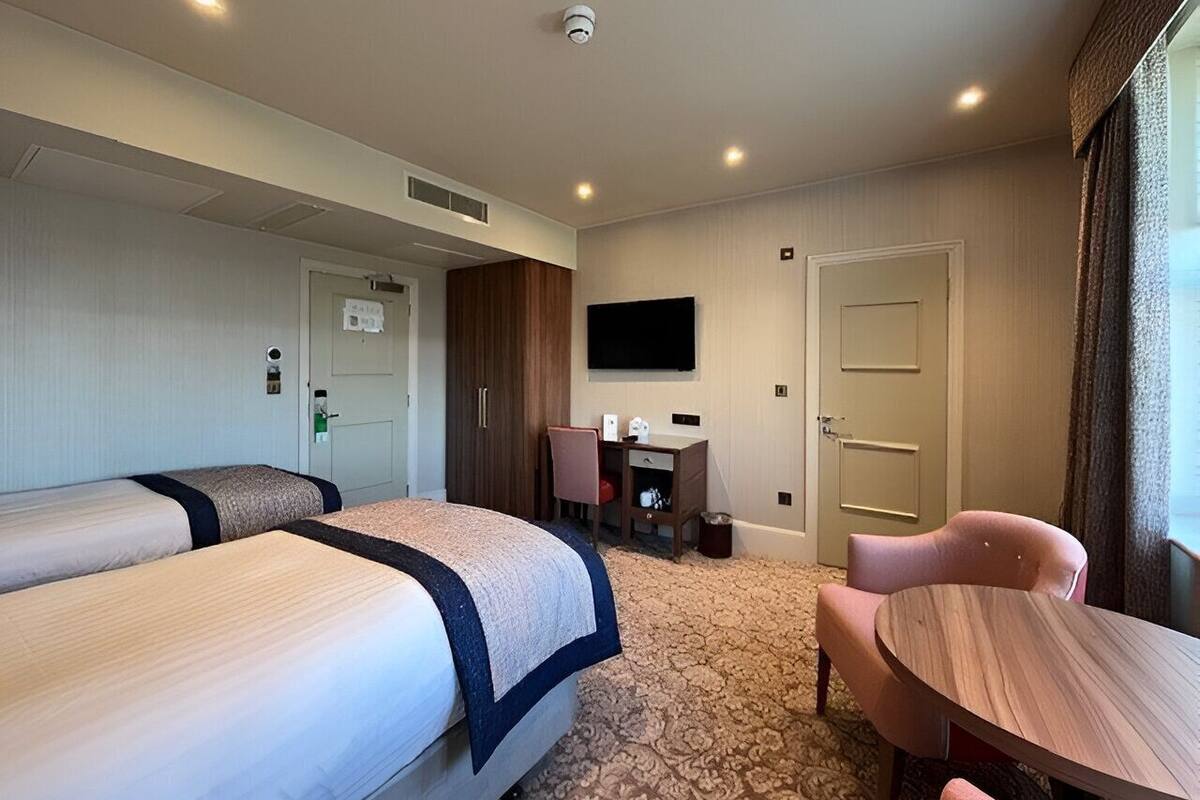 Une chambre d’hôtel avec deux lits, un bureau, une chaise, une télévision et une porte.