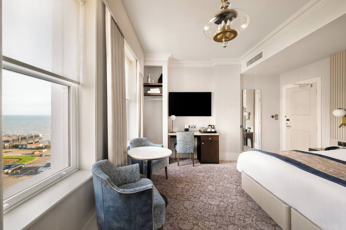 Une chambre d’hôtel équipée d’un lit, d’un bureau, d’une chaise, d’une petite table et d’un téléviseur.