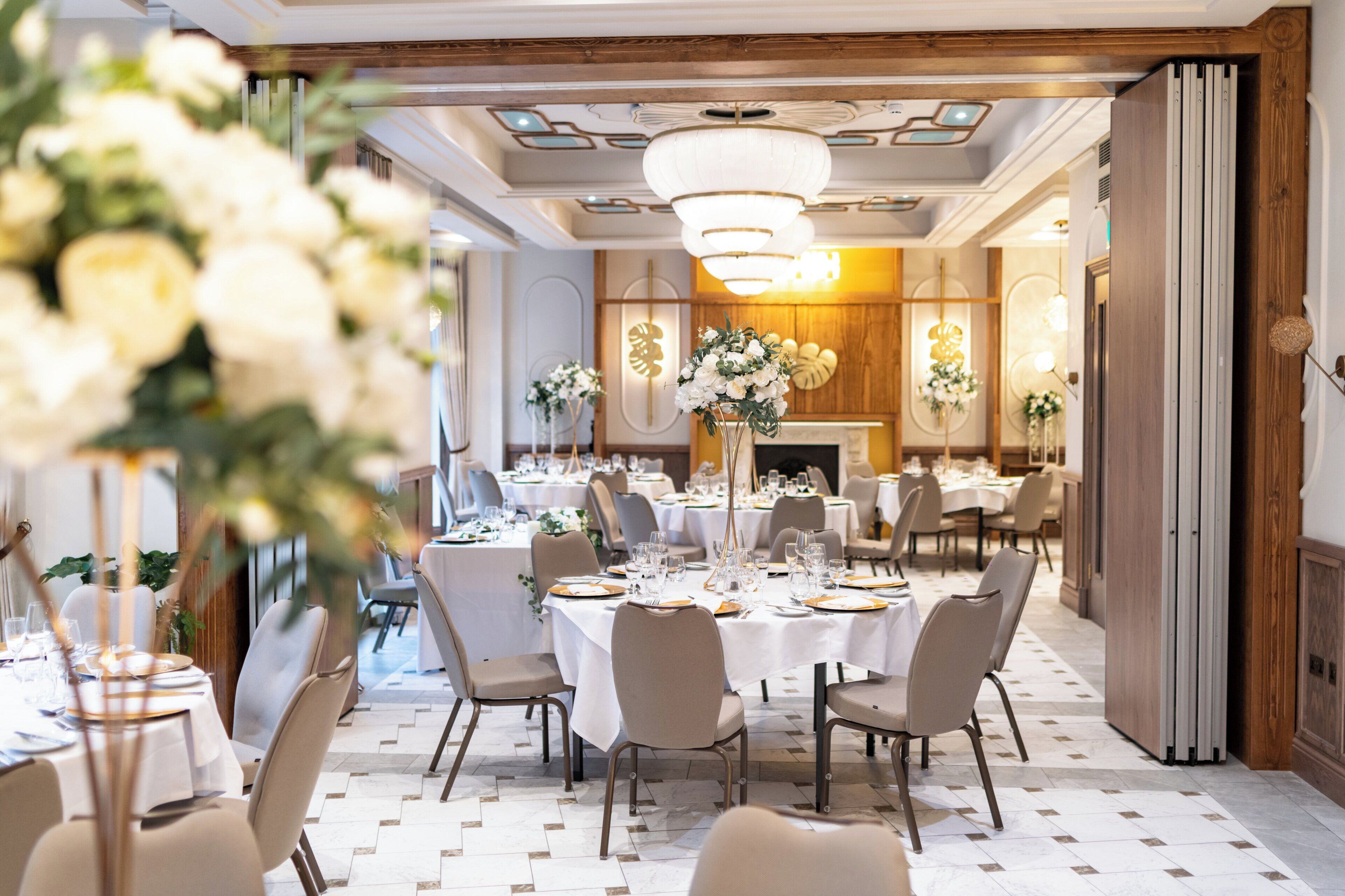 Ein formeller Speisesaal mit runden Tischen, gedeckt für mehrere Gäste, mit einem zentralen Blumenarrangement und stilvollen Leuchten.