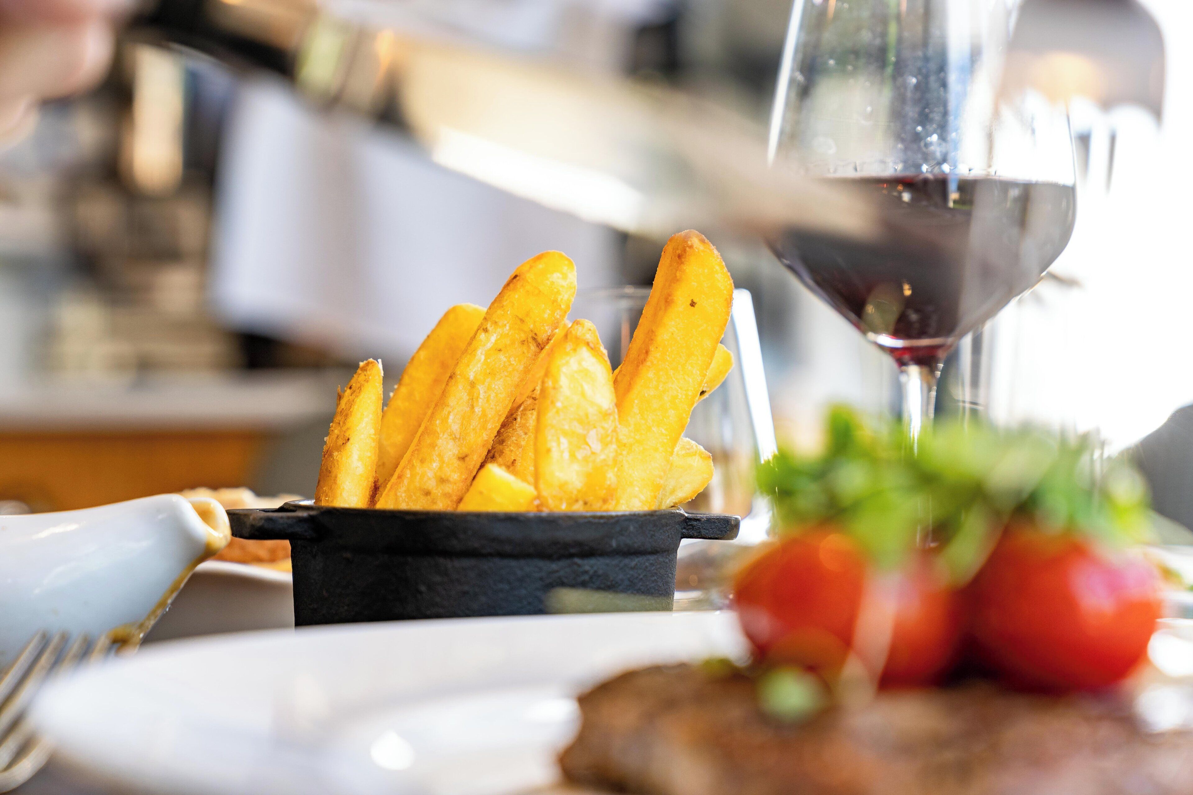A plate of golden fries, a glass of red wine, and fresh tomatoes on a table.