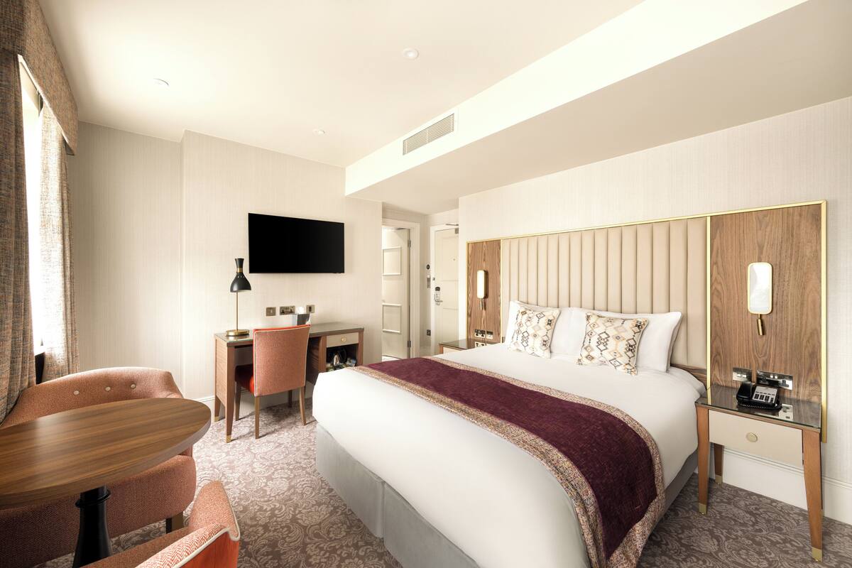 Une chambre d’hôtel avec un grand lit, un bureau, une chaise et un téléviseur fixé au mur.