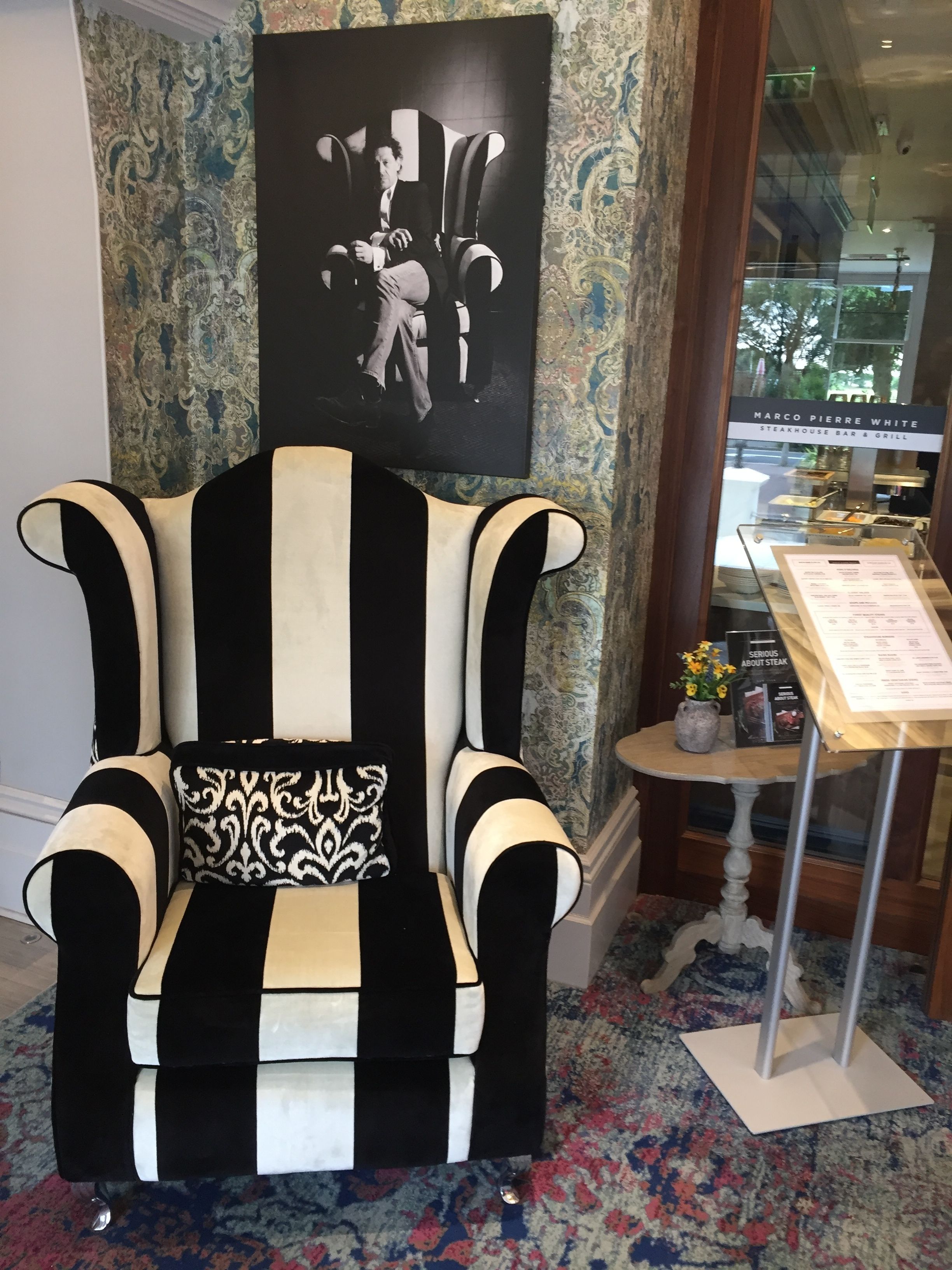 A black and white striped armchair with a patterned pillow, positioned in front of a wall with a large framed picture and a glass display case with a menu.
