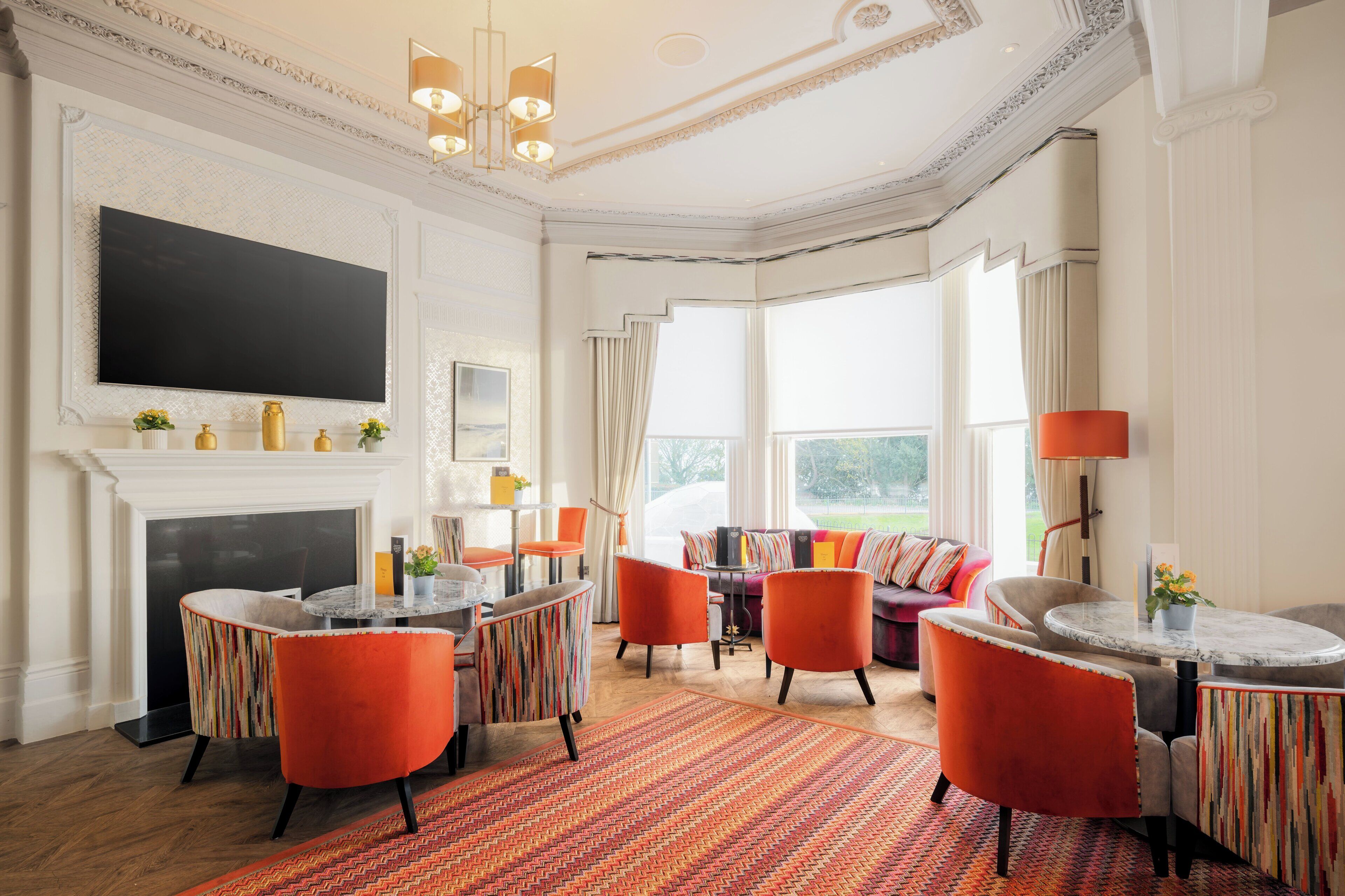A spacious living room with a fireplace, a large flat-screen TV, and a comfortable seating area with orange chairs and a sofa.