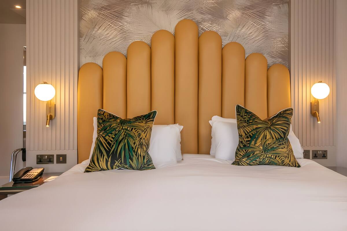 Une chambre d’hôtel avec un grand lit, deux coussins décoratifs, un luminaire fixé au mur et un téléphone sur la table de chevet.