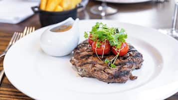 Un bistec acompañado de papas fritas y un recipiente pequeño con salsa sobre un plato blanco.