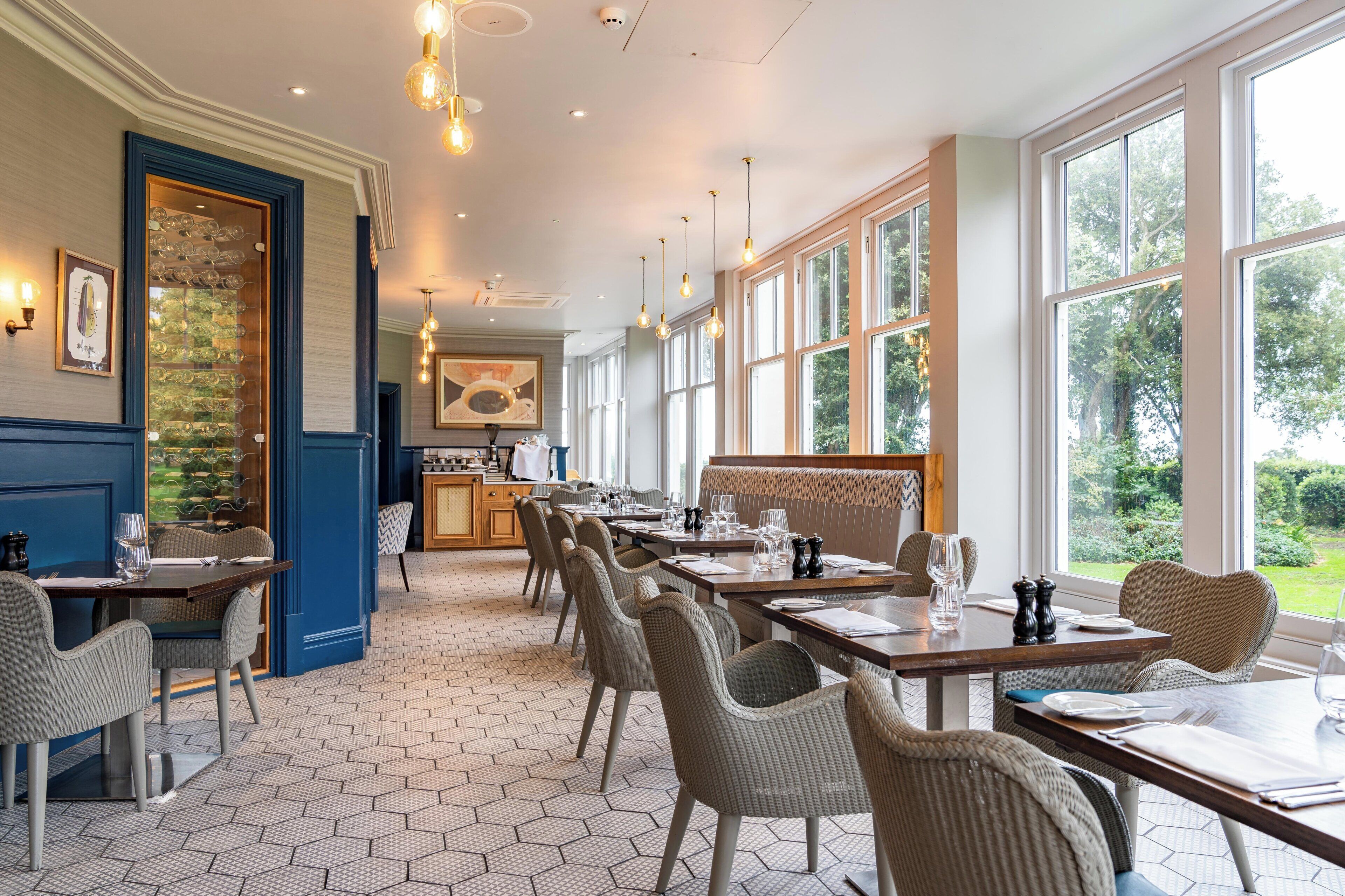A restaurant with hexagonal tiled flooring, wicker chairs, and tables set for dining.