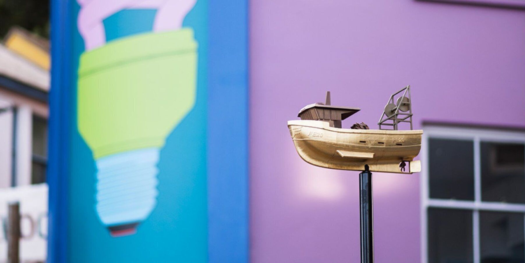 A model boat on a pole with a colorful mural in the background.
