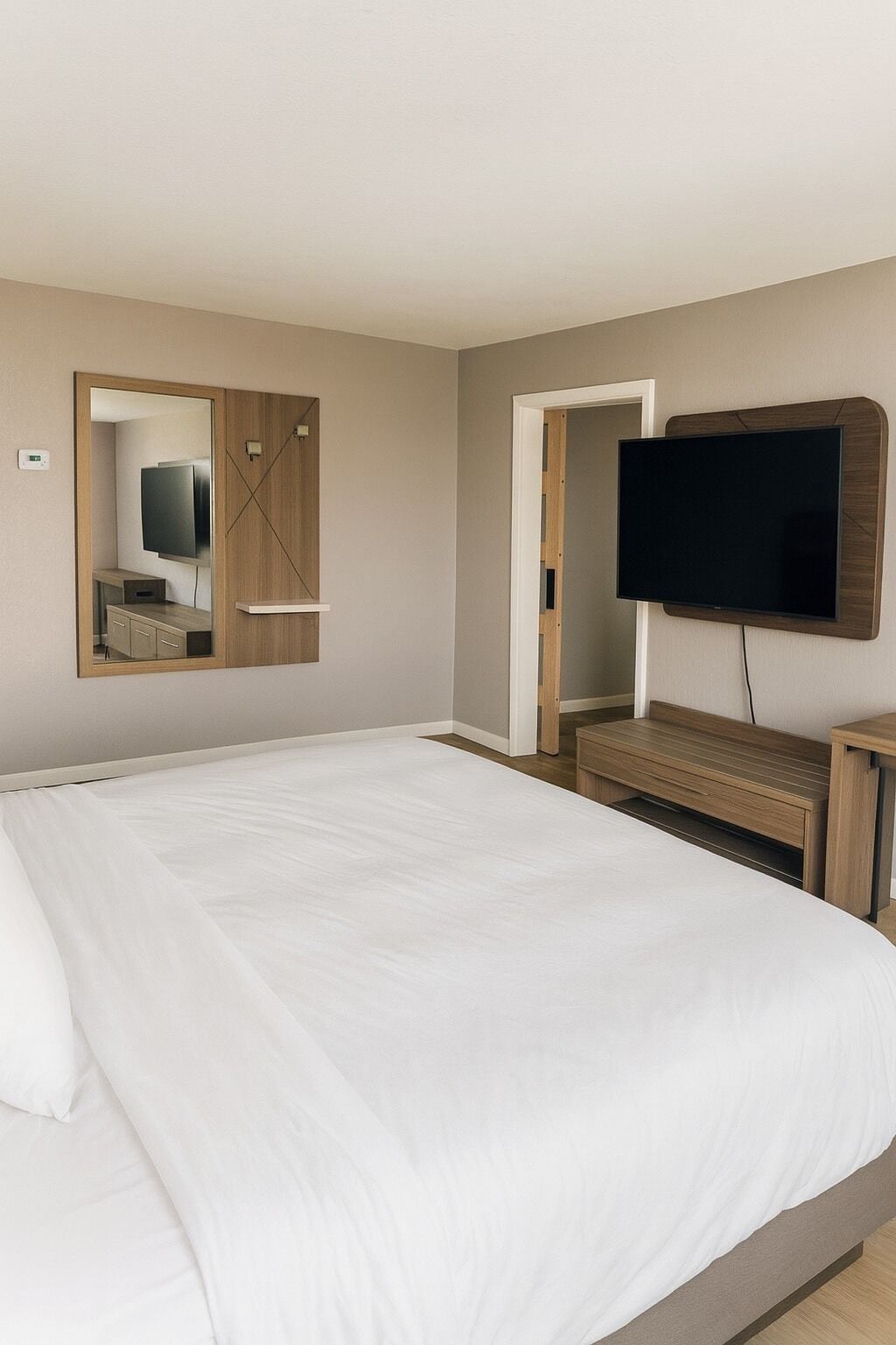 A hotel room with a large bed, a TV mounted on the wall, and a wooden wardrobe.