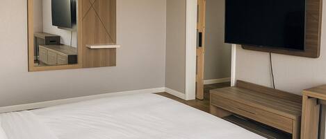 A hotel room with a large bed, a TV mounted on the wall, and a wooden wardrobe.
