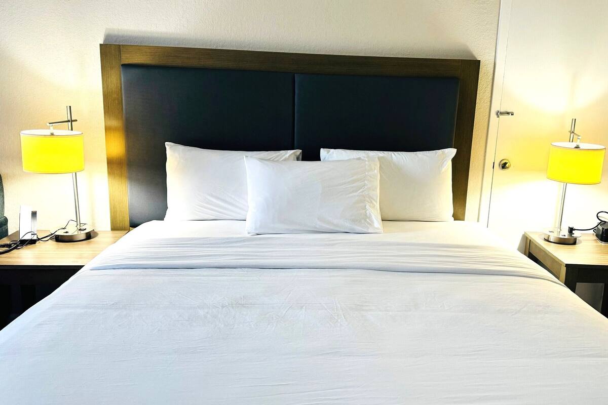 A hotel room with a large bed, two bedside tables, a wooden headboard, and two bedside lamps.