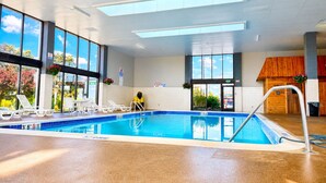 Una piscina interior con paredes de vidrio transparente, suelo de baldosas y una estructura de madera al fondo.