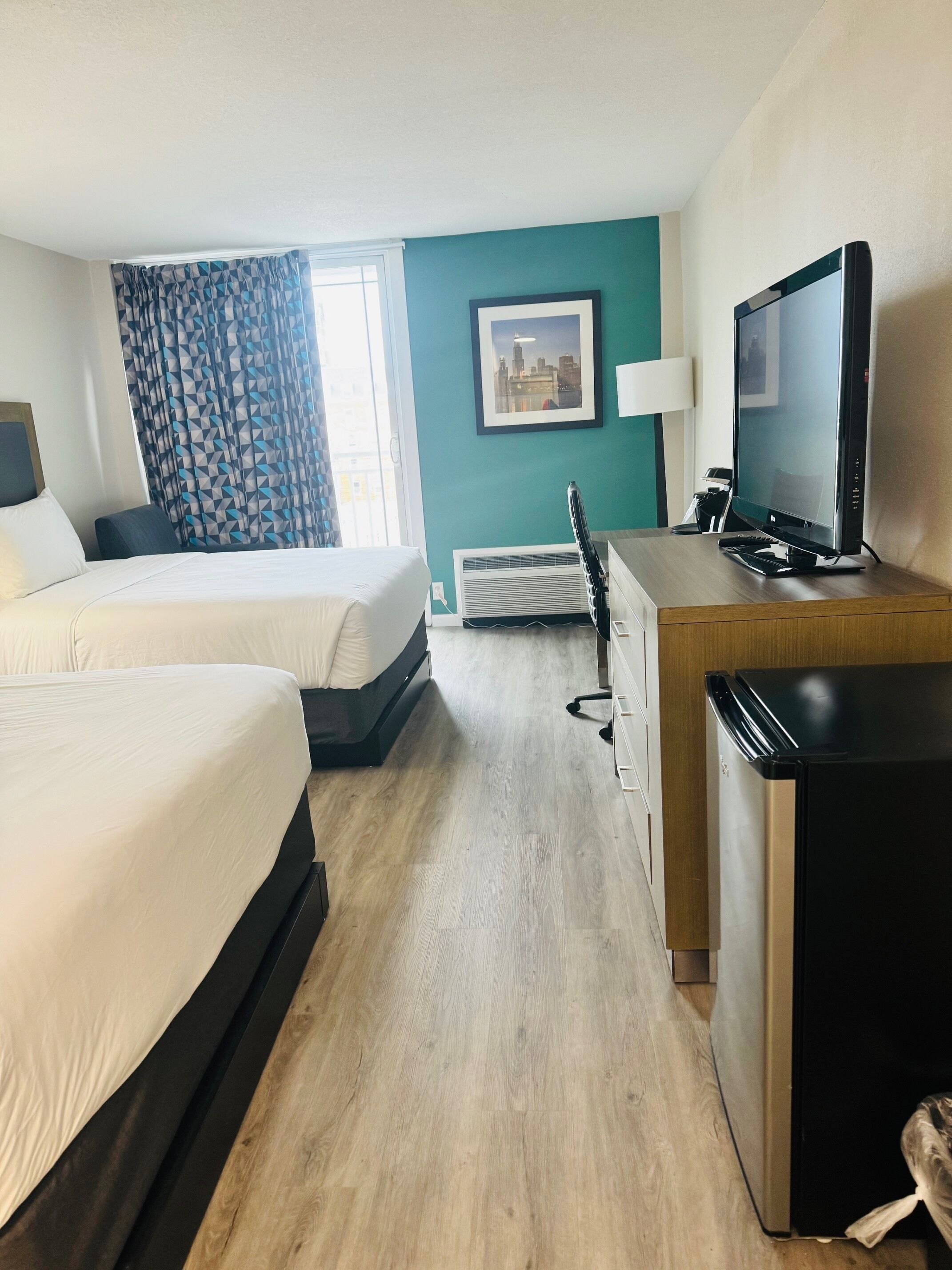 Habitación de hotel con dos camas, un escritorio, televisión, una silla y ventana con cortinas.