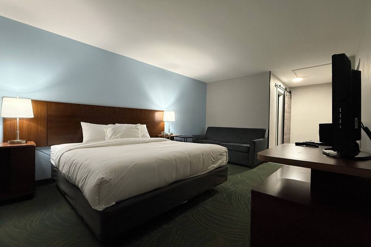 A hotel room with a bed, bedside tables, a desk, a chair, a TV, and a lamp.