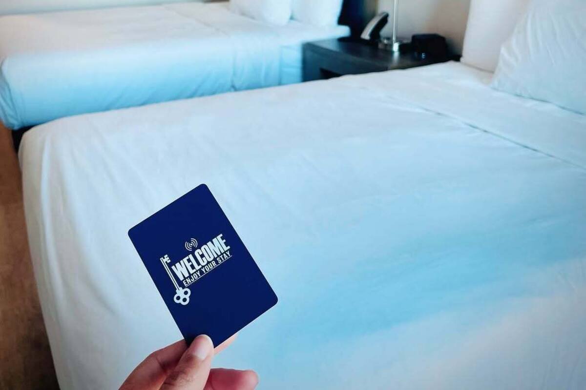 A hotel room with two beds, a nightstand with a lamp, and a framed picture on the wall.