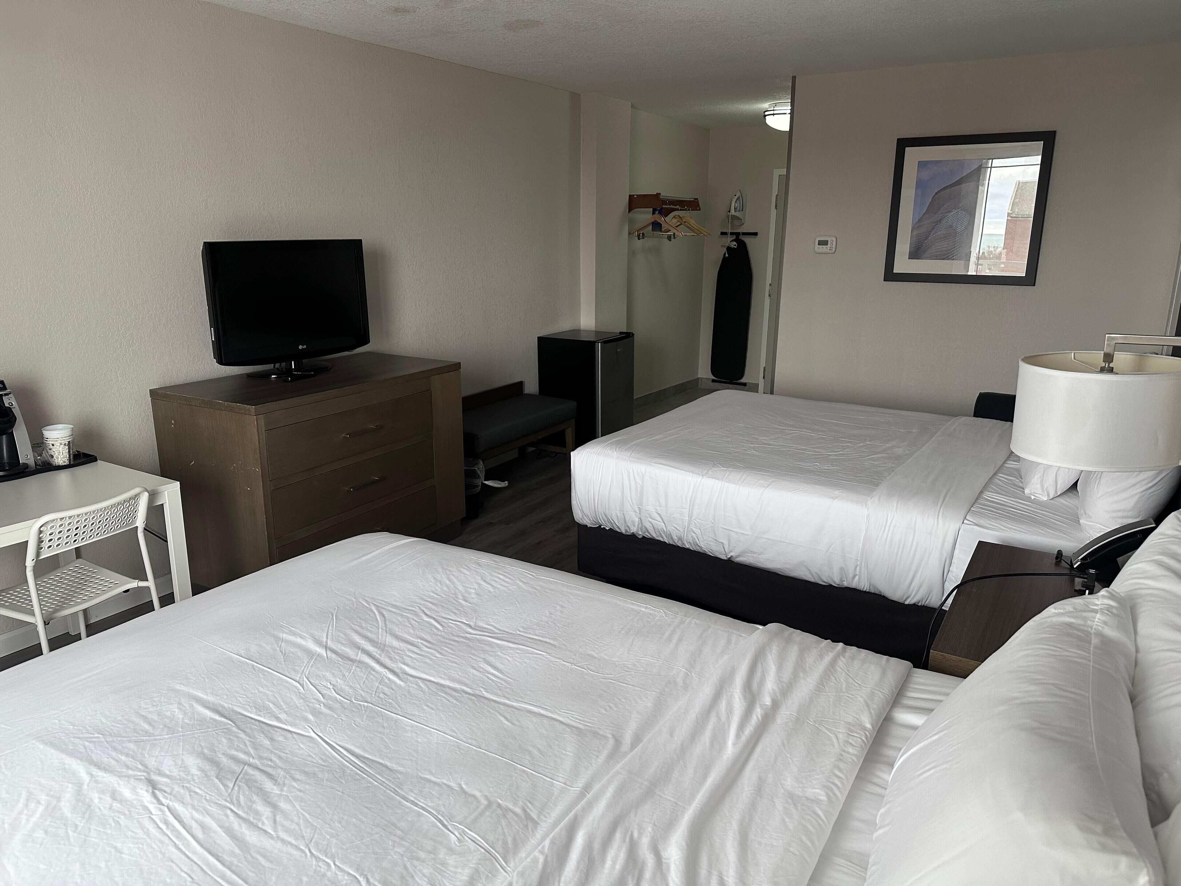 A hotel room with two beds, a TV, a desk, and a mirror.