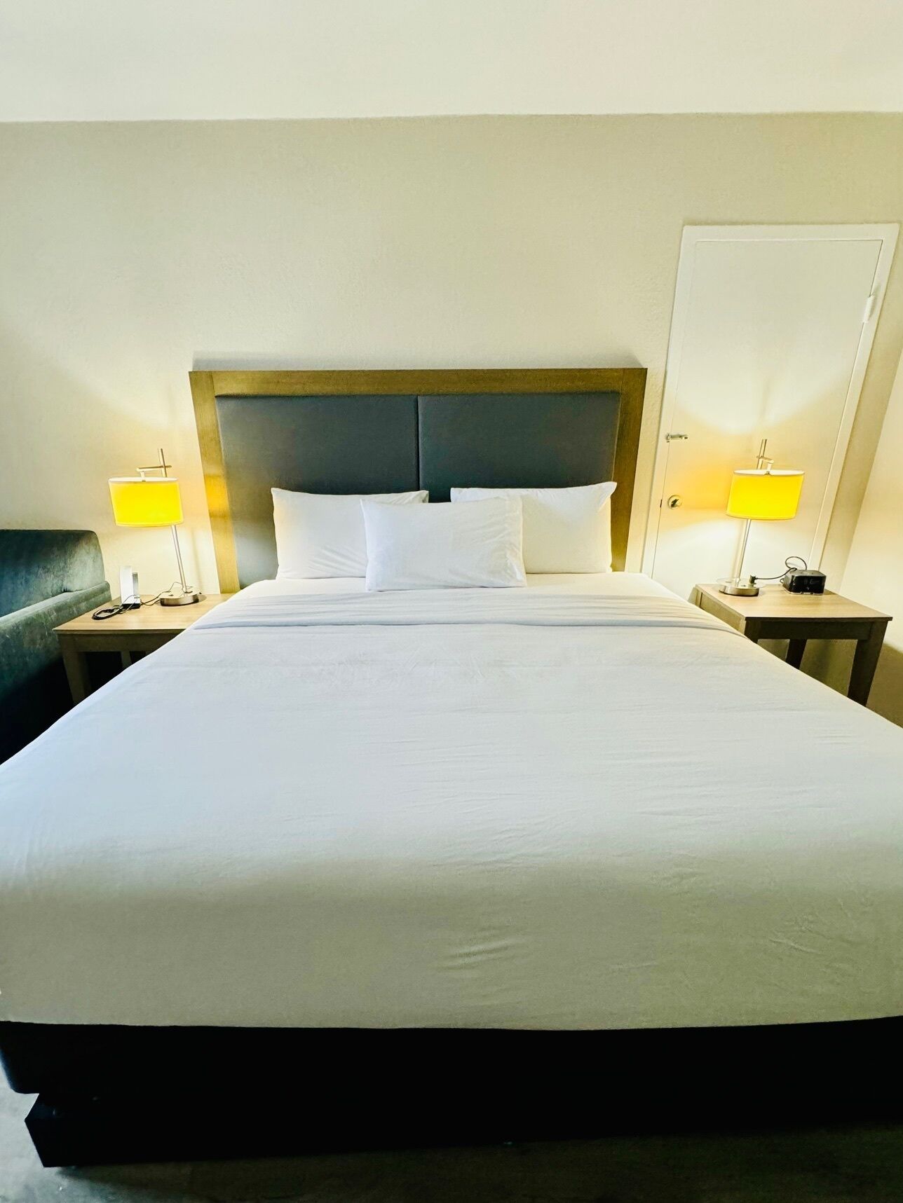 A neatly made bed with white linens and a wooden headboard. There are two bedside tables, each with a lamp and a small table.