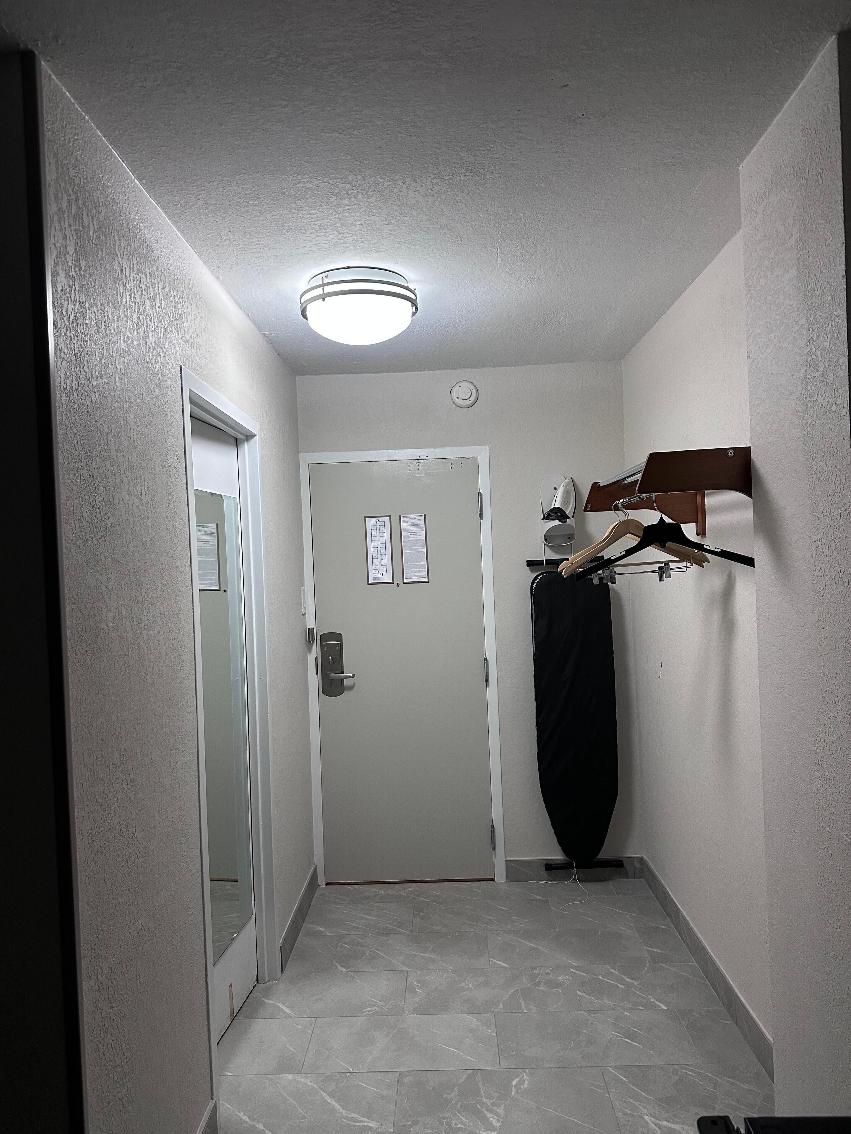 A narrow hallway with a white door, a coat rack with hangers, and a ceiling light fixture.