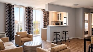 Una sala moderna con un sofá, un reposapiés y una pequeña cocina con microondas y taburetes.