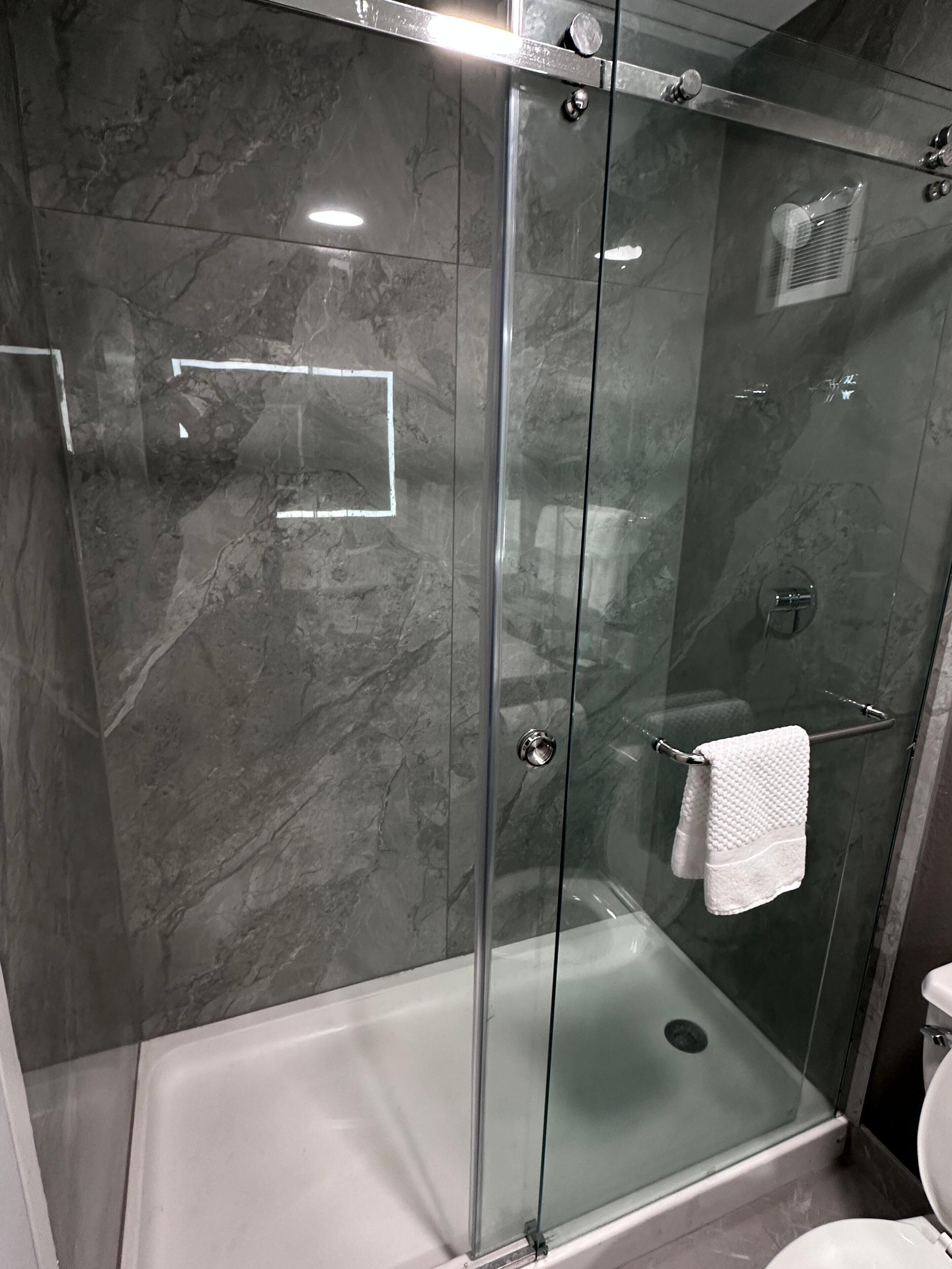 A glass-enclosed shower stall with a white bathtub and a towel rack.