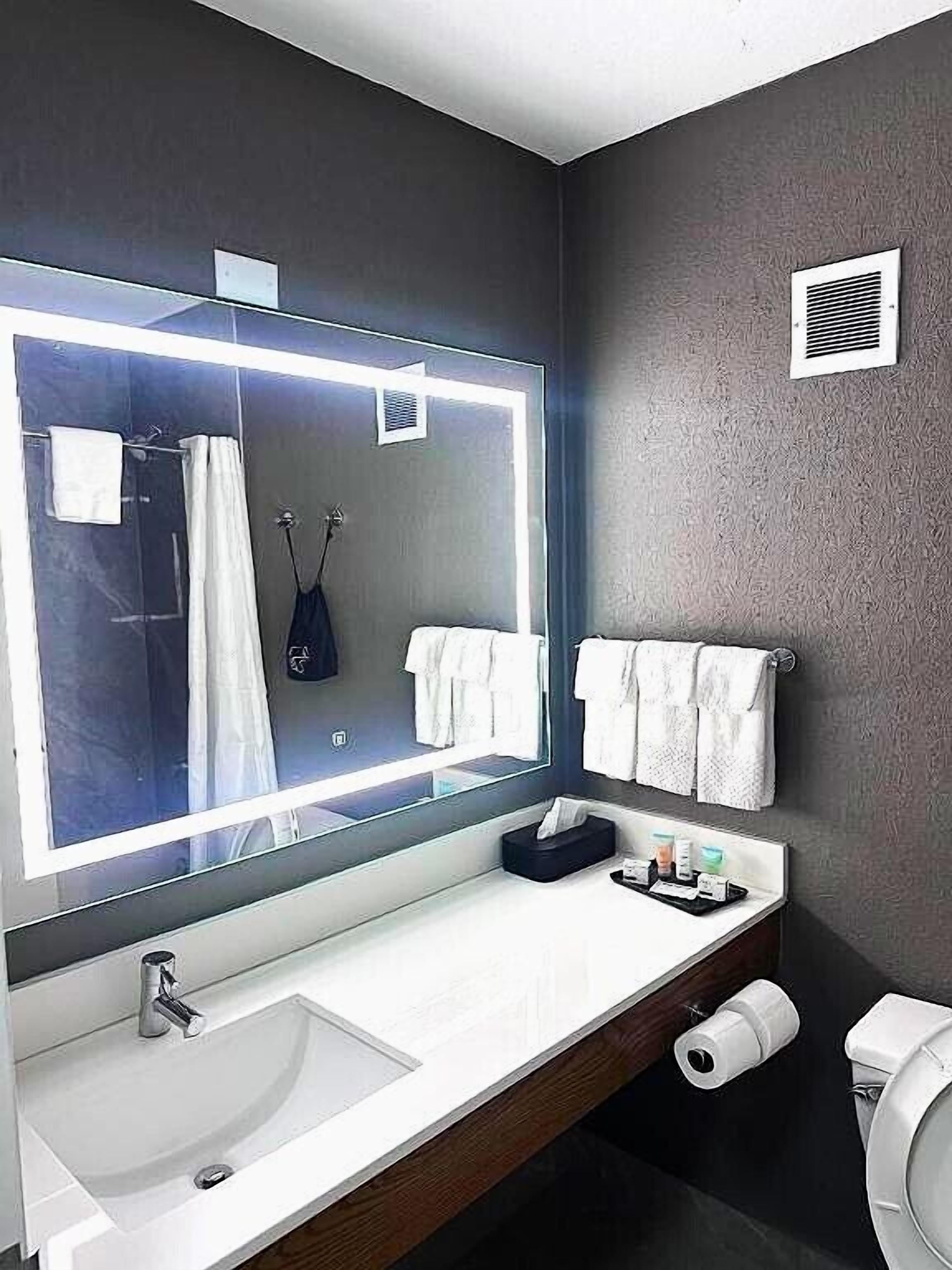 A modern bathroom with a large mirror, white sink, and a toilet.