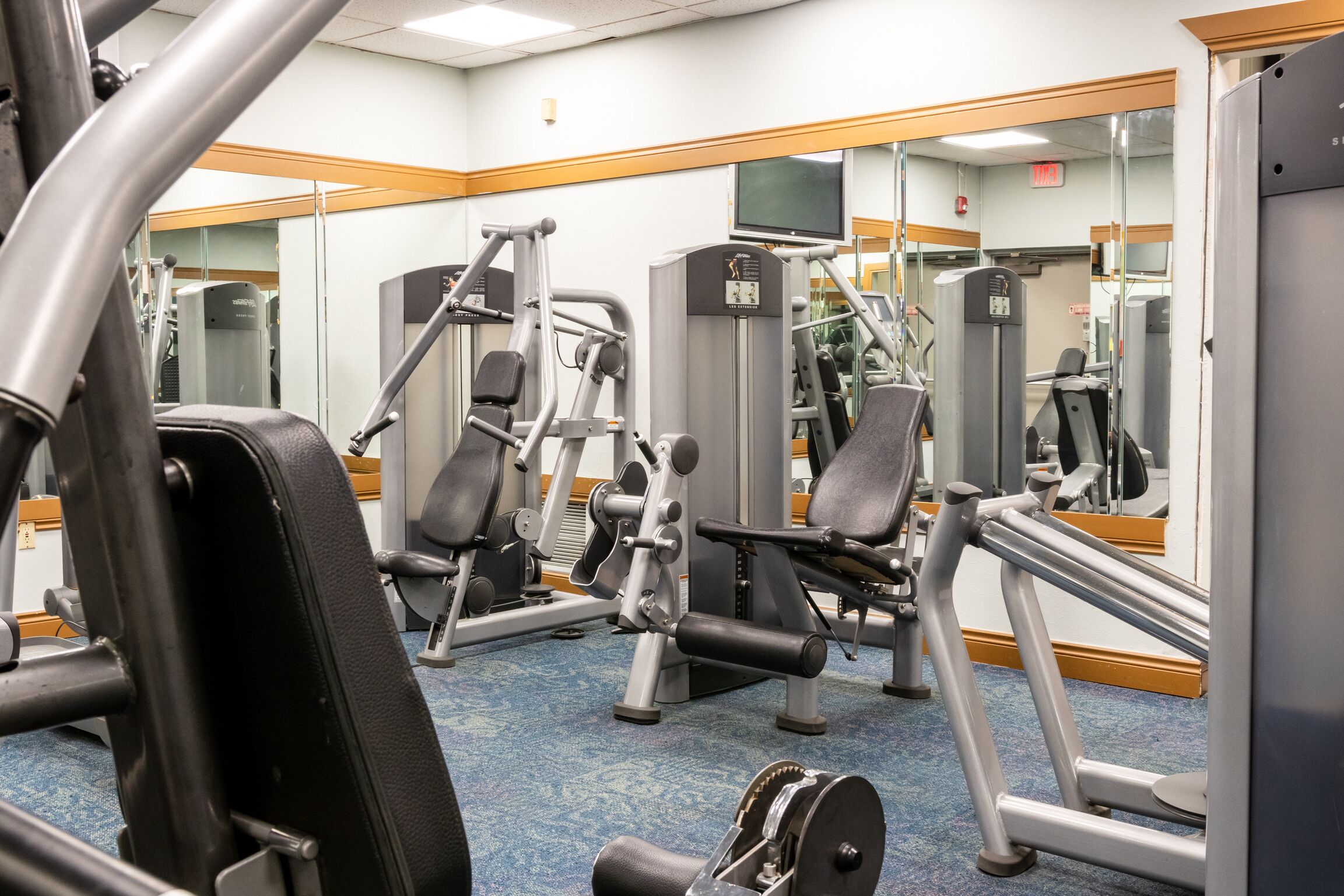 A gym with various exercise machines, a large mirror, and a carpeted floor.