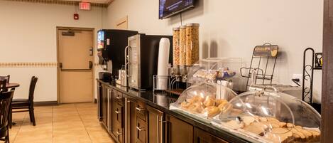 Een buffetgedeelte met een koelkast, koffieapparaten en een televisiescherm.