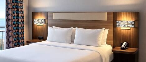 Una habitación de hotel moderna con una cama grande, cabecera de madera y dos mesitas de noche con lámparas.