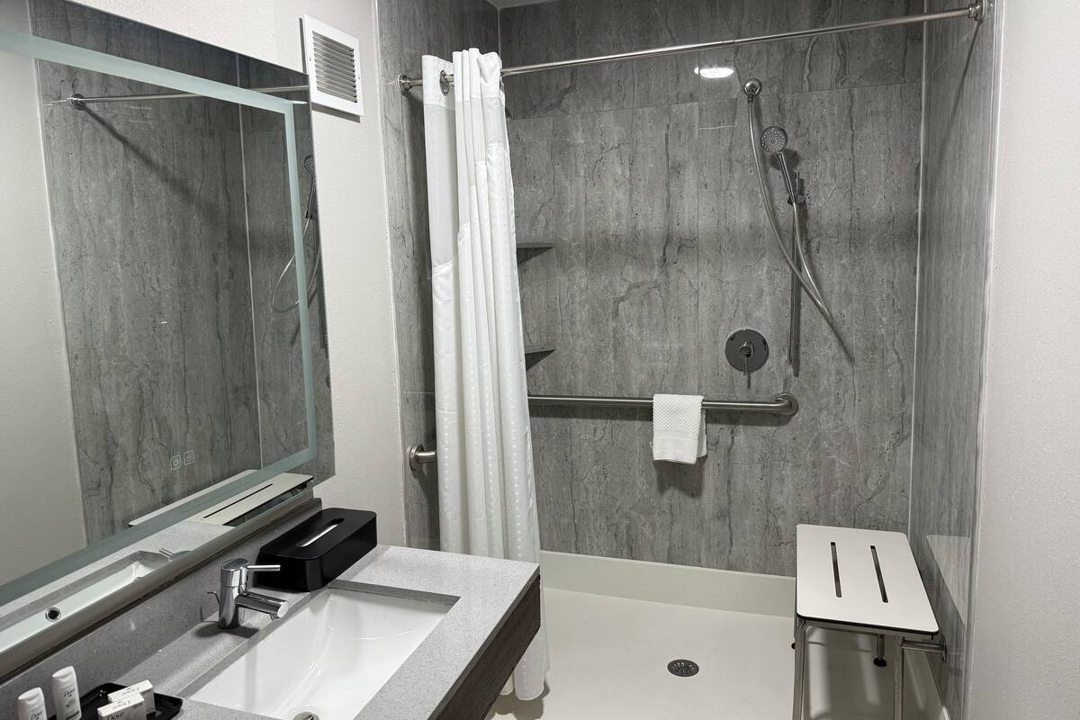 A modern bathroom with a large mirror, a sink, a shower with a glass door, and a small stool.