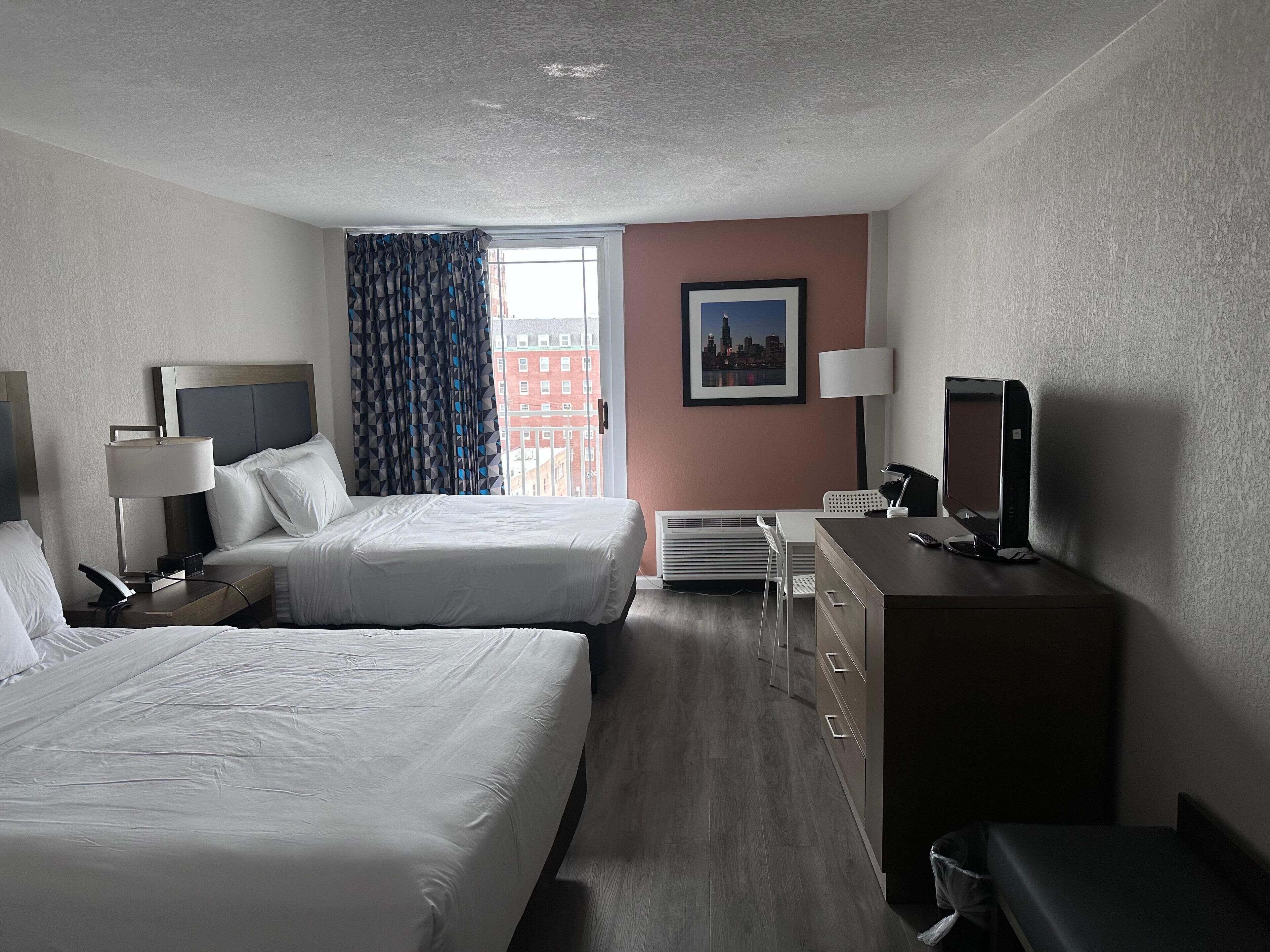 A hotel room with two beds, a desk, a chair, a television, and a window with curtains.