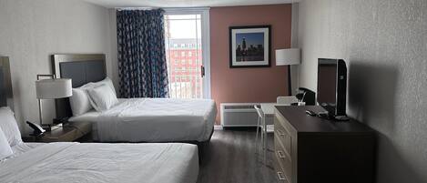 A hotel room with two beds, a desk, a chair, a television, and a window with curtains.