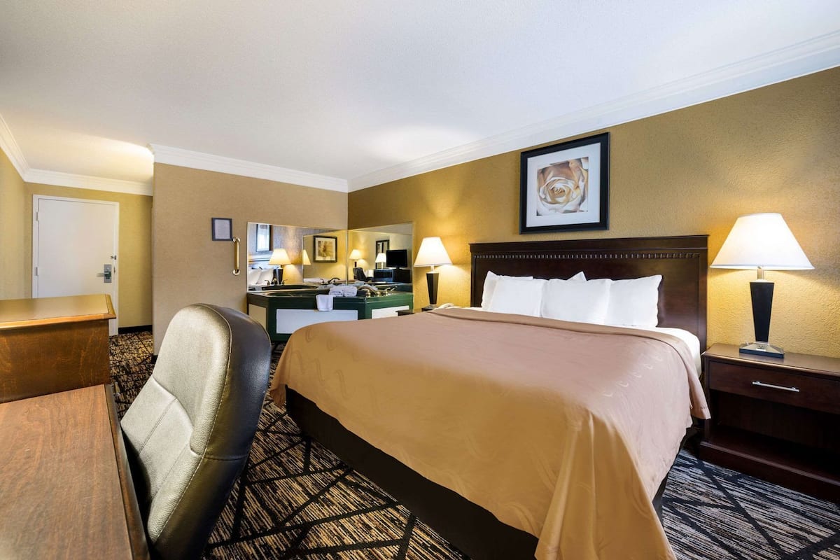 A hotel room with a bed, a desk, a chair, a dresser, a mirror, and a bathroom.