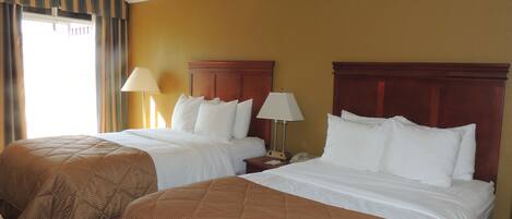 A hotel room with two beds, each with a wooden headboard, white bedding, and a brown quilted bedspread. There is a nightstand with a lamp and a telephone on each bed.