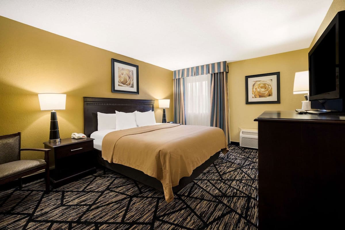 A hotel room with a bed, a desk, a chair, a television, and two framed pictures on the walls.