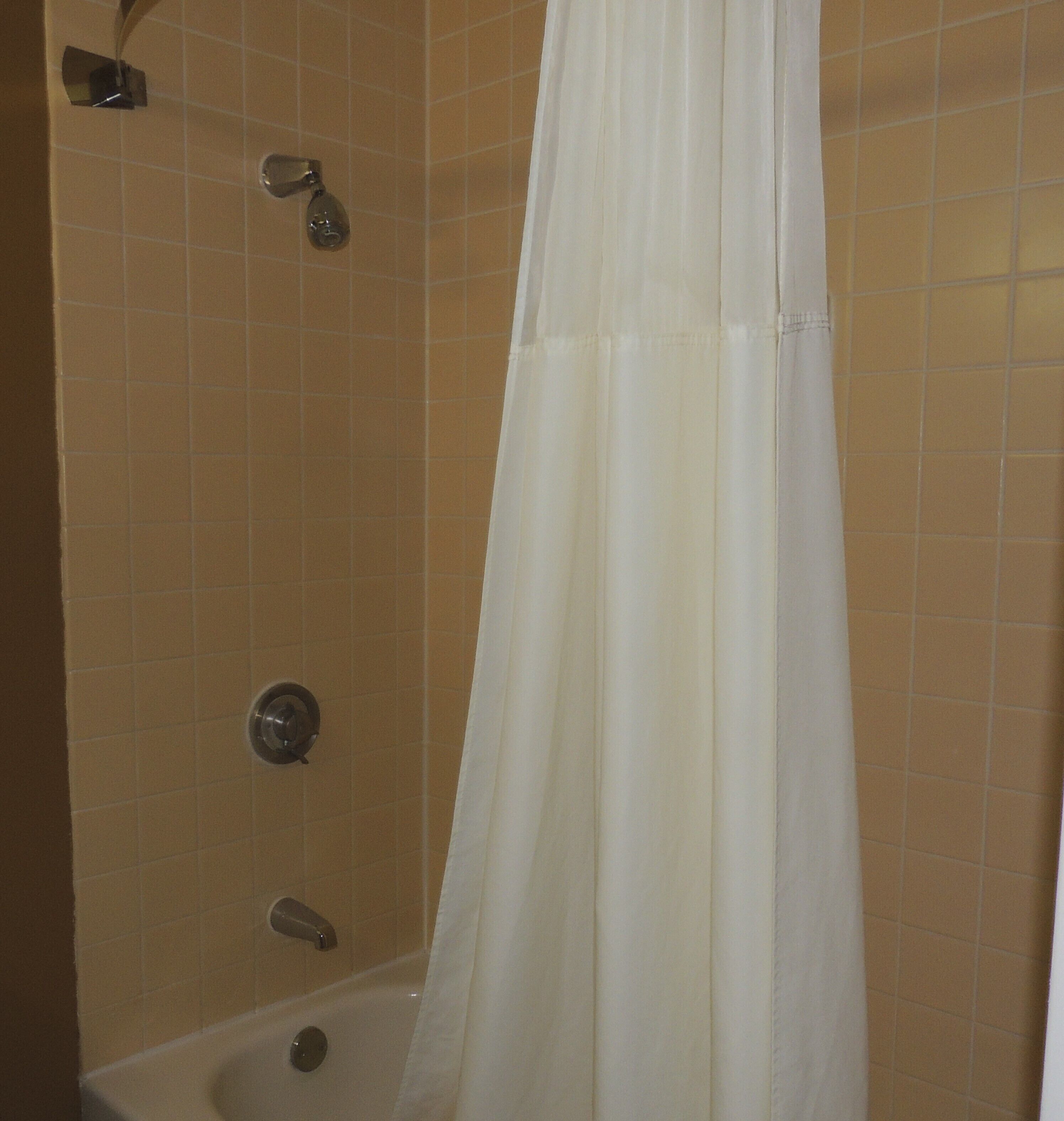 A shower area with a white shower curtain, a handheld showerhead, and a wall-mounted faucet.