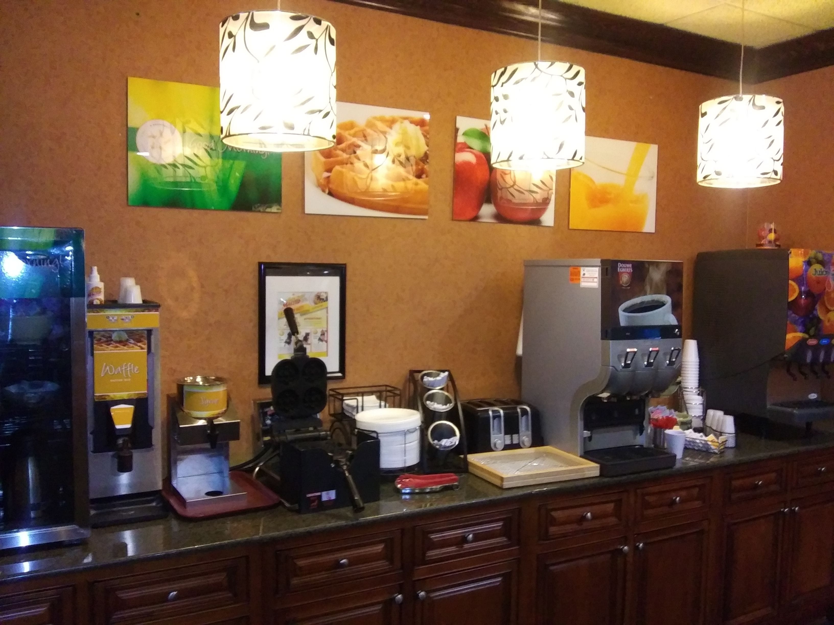 A breakfast bar with waffle and juice dispensers, a coffee maker, and a toaster.