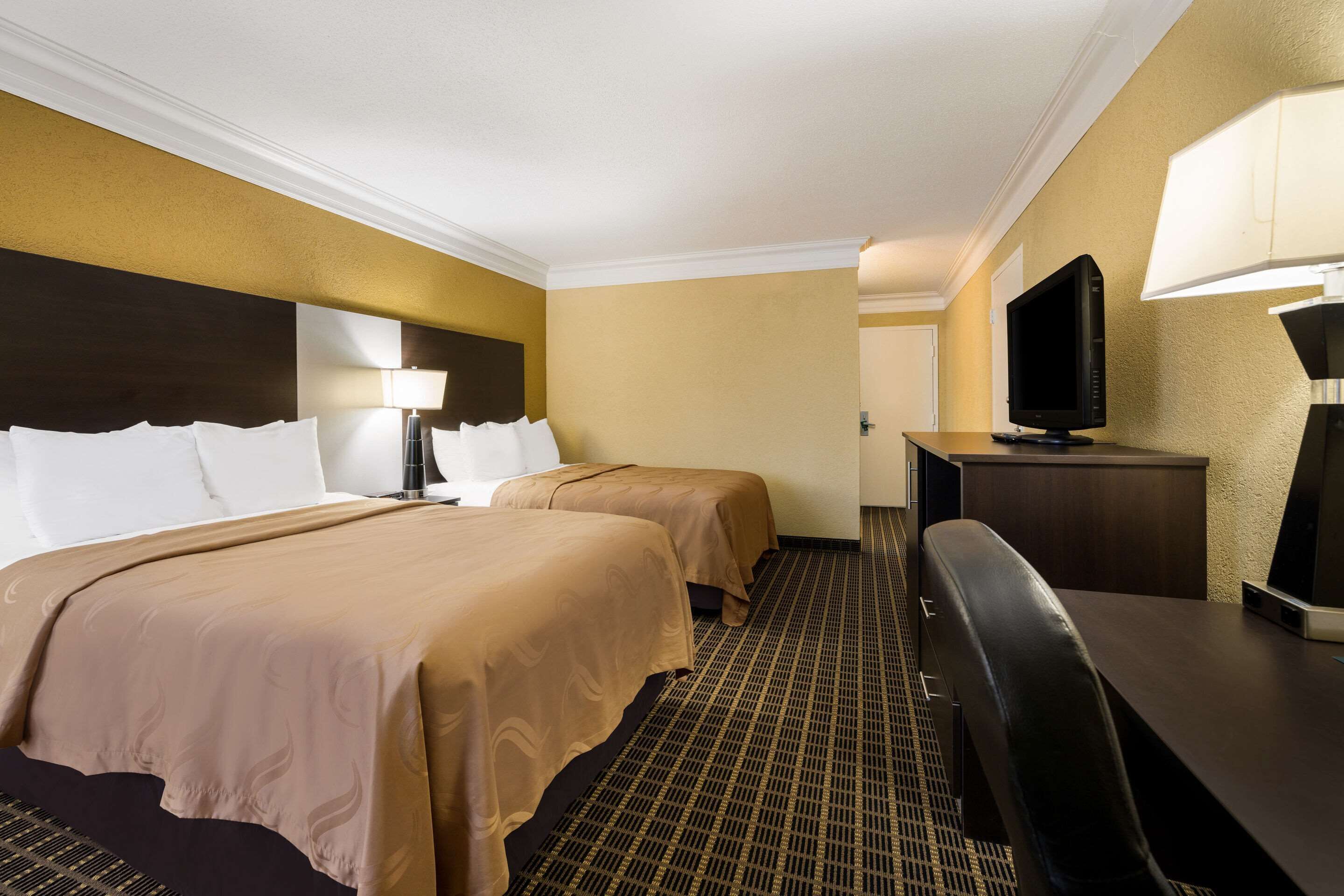Une chambre d’hôtel avec deux lits, un bureau, une télévision et une lampe.