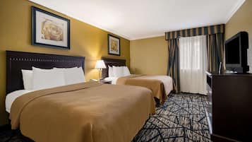 A hotel room with two beds, a TV, a desk, and a lamp.