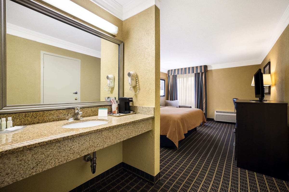 A hotel bathroom with a granite countertop sink, a large mirror, a hairdryer, and a coffee maker.