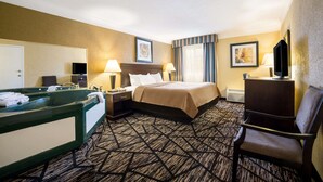 A hotel room with a large bed, a desk with a chair, a vanity with a mirror, and a television.