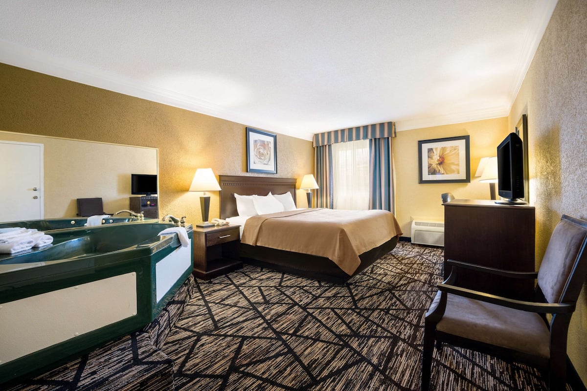 A hotel room with a large bed, a desk with a chair, a vanity with a mirror, and a television.