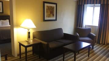 A hotel room with a bed, a sofa, a chair, a small table, a lamp, and a window with curtains.