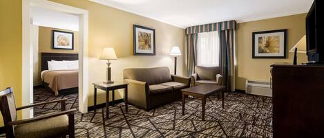 A hotel room with a bed, a sofa, a chair, a small table, and a TV.