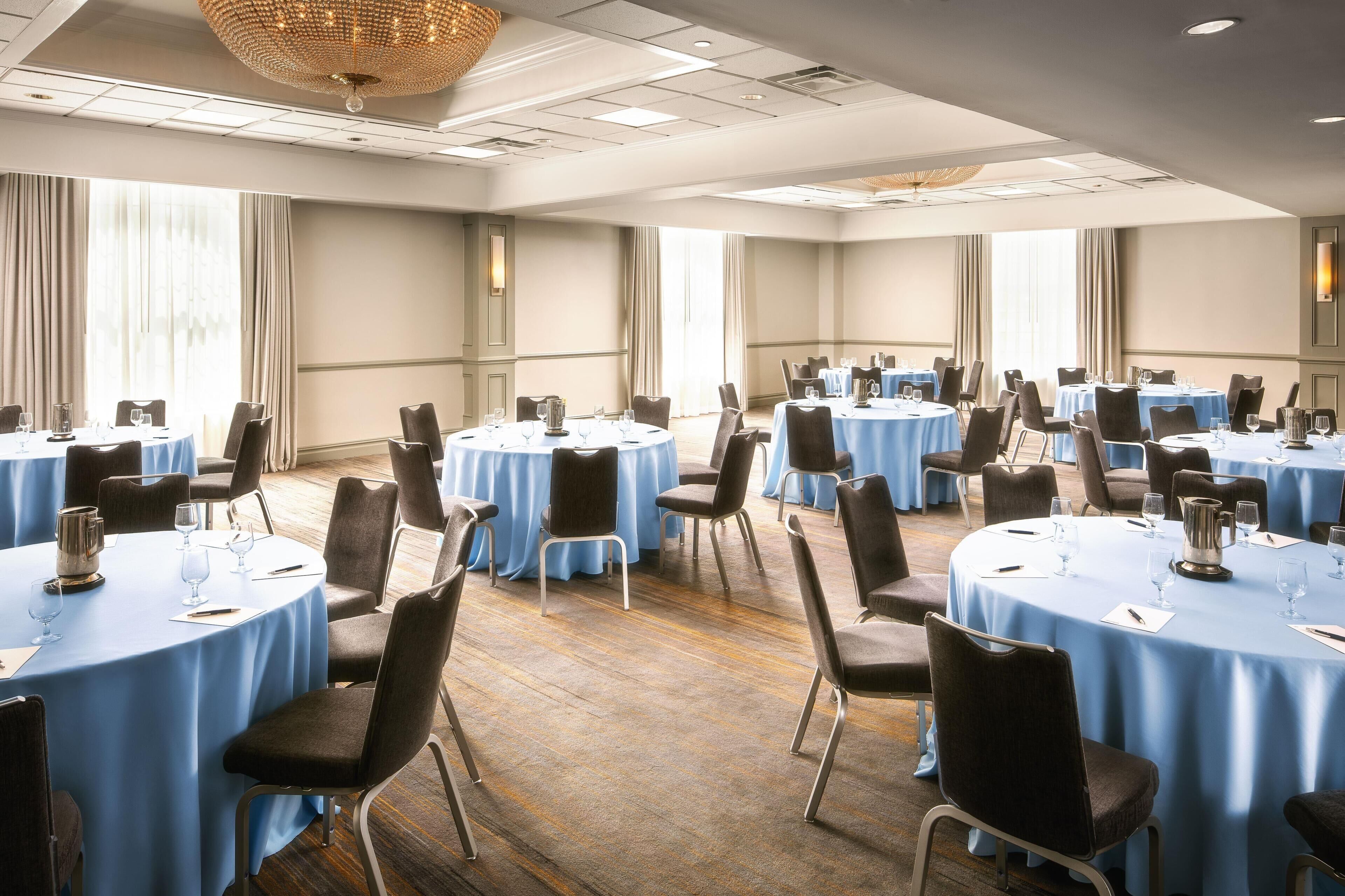 A conference room with round tables, chairs, and a chandelier.