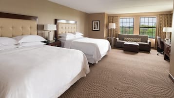 A hotel room with two beds, a sofa, a desk, and a view of the outdoors.