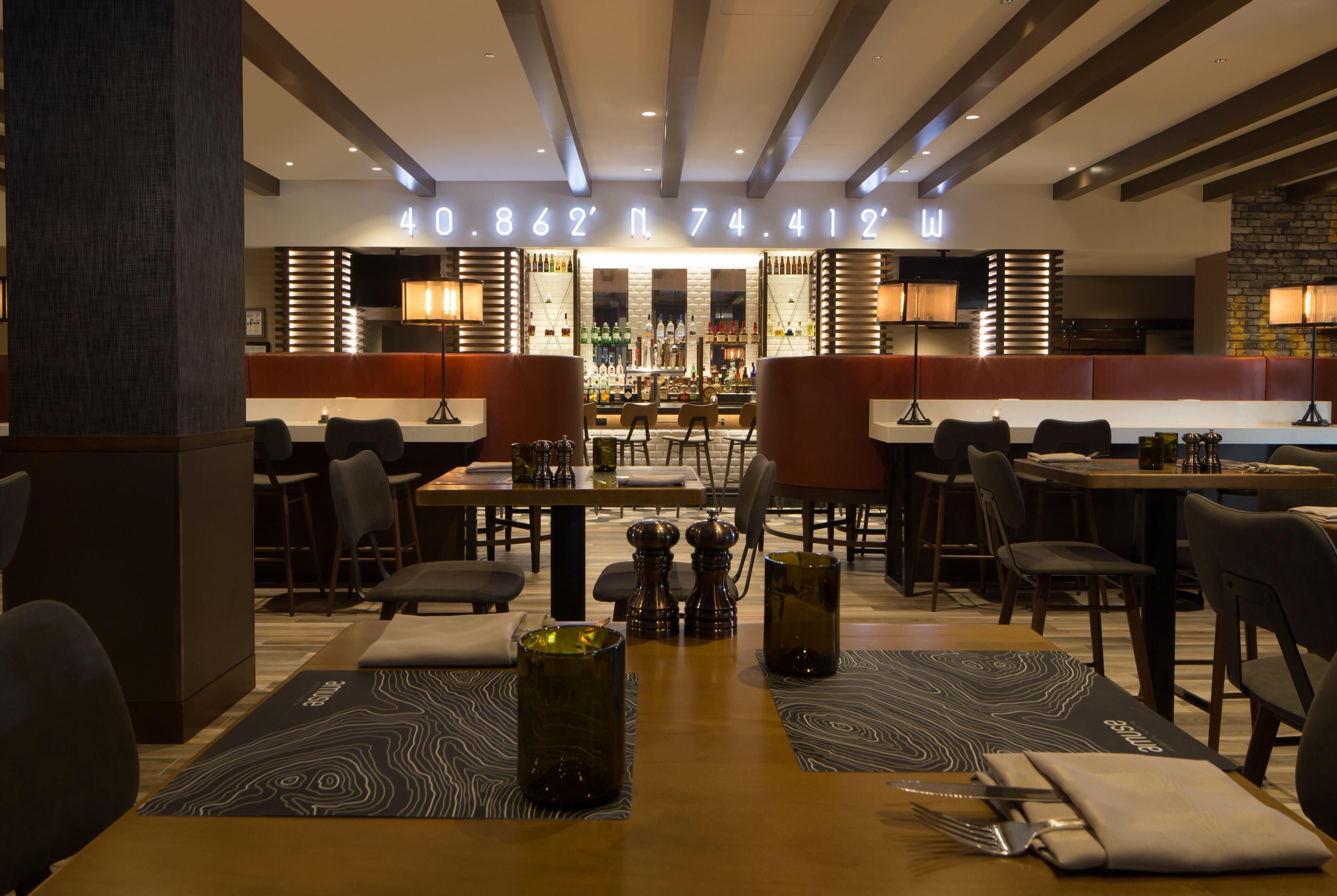 Um restaurante com área de bar, mesas com cadeiras e um balcão de bar com garrafas.