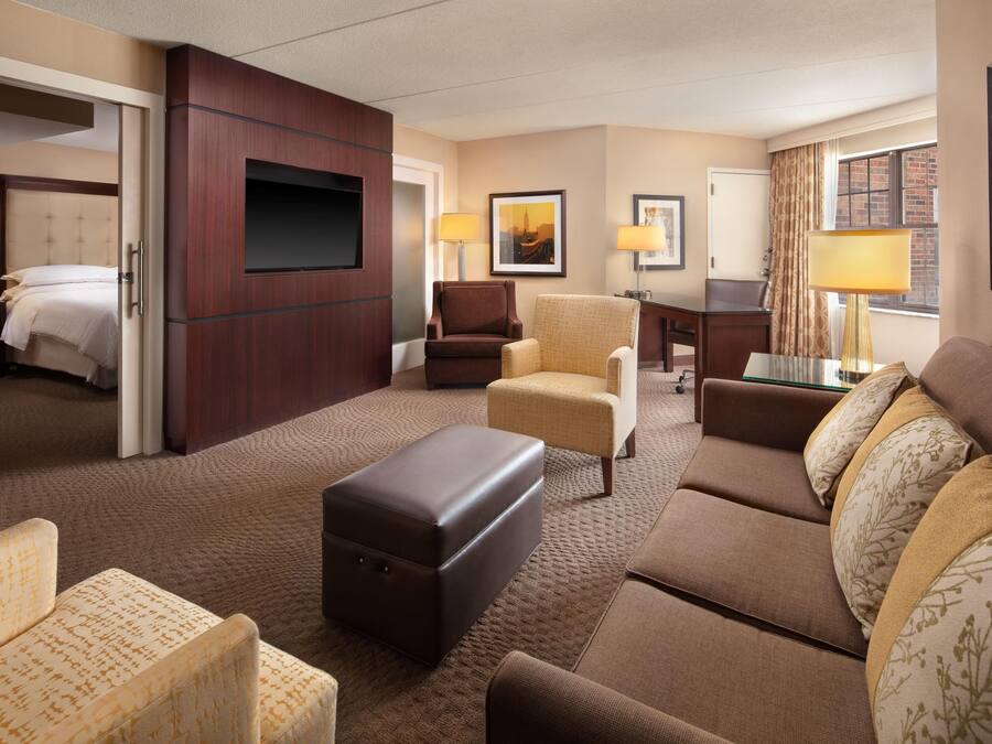 A hotel room with a bed, a seating area with a sofa and chairs, a small table, a TV, and a desk.