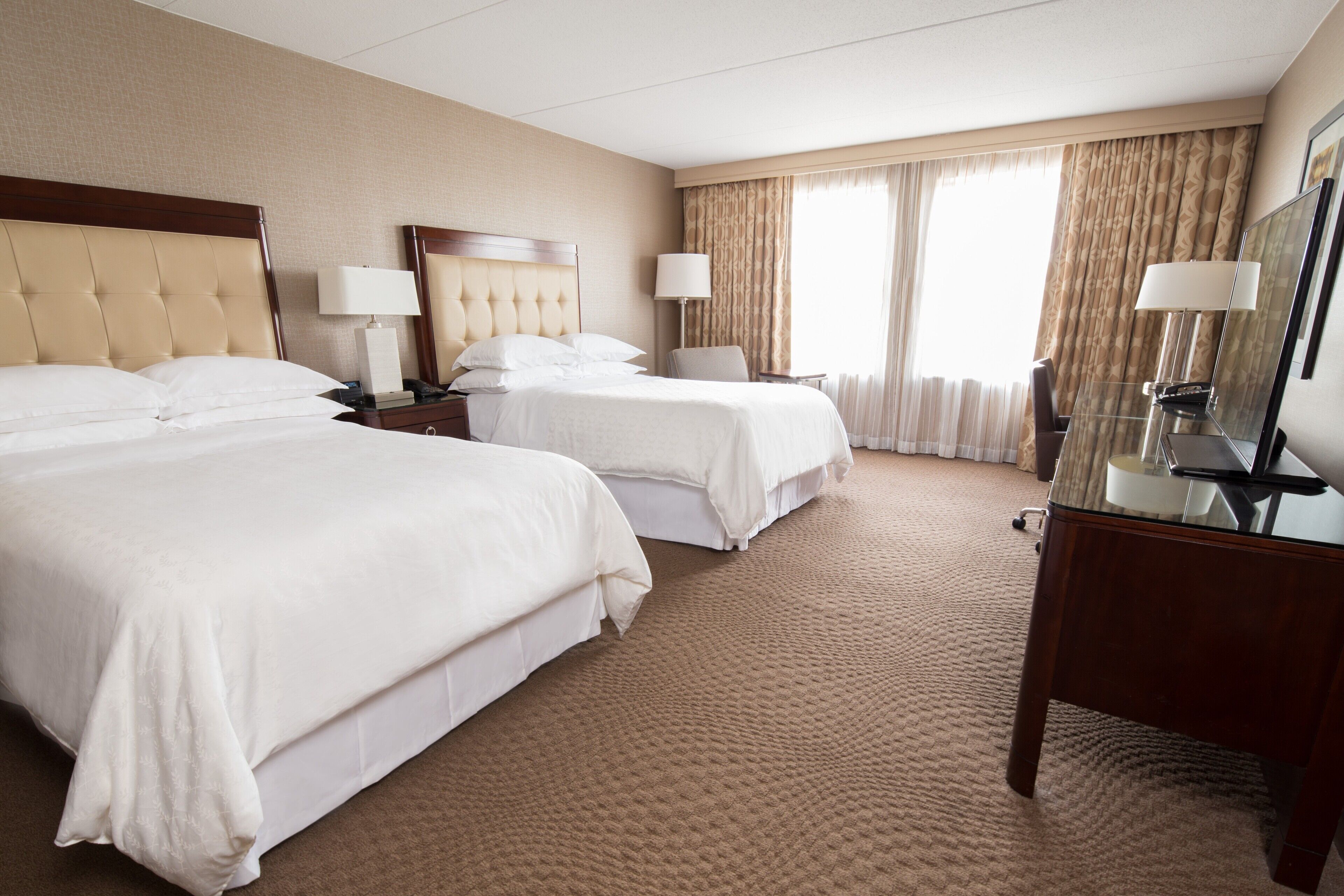 A hotel room with two beds, a large mirror, a desk, and a window with curtains.